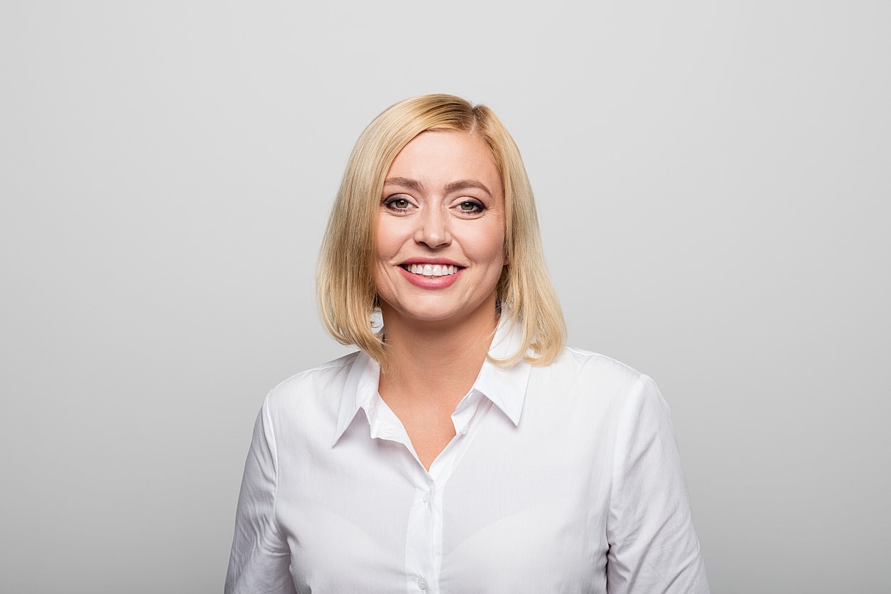 Smiling woman in white shirt against gray background.